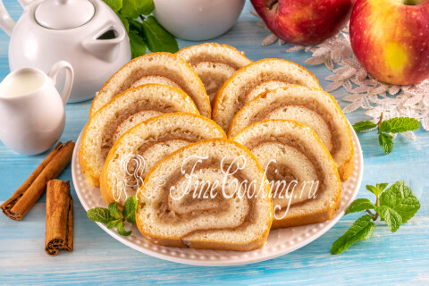 Бисквитный рулет с яблоками нарезан кусочками на тарелке.