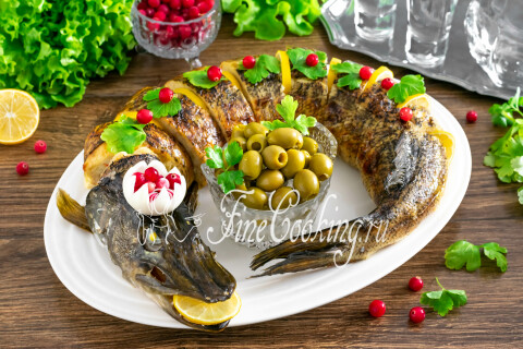 Фаршированная щука на блюде украшена дольками лимона, петрушкой и клюквой в форме целой рыбы.