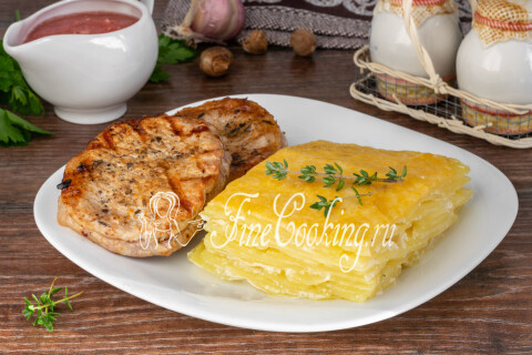 Картофельный гратен, нарезанный порционными кусочками, на тарелке.