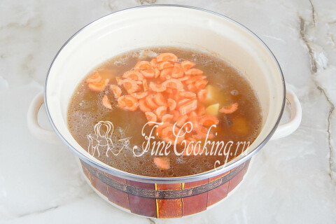 Кусочки картофеля и моркови варятся в кастрюле с грибным супом.