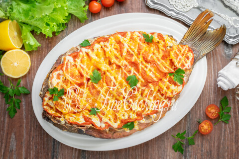 Запечённый карп под помидорами, сметаной и сыром, украшенный петрушкой.