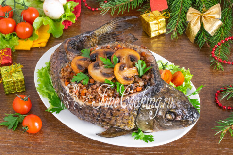 Запечённый карп с гречкой и грибами на блюде, украшенный зеленью и грибами.
