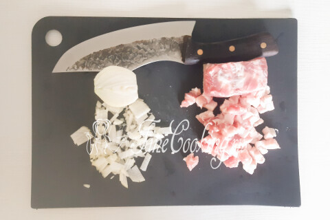 Свиная грудинка и репчатый лук, нарезанные мелким кубиком на доске.