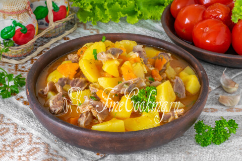 Картошка с куриными желудочками на тарелке, посыпанная свежей зеленью.