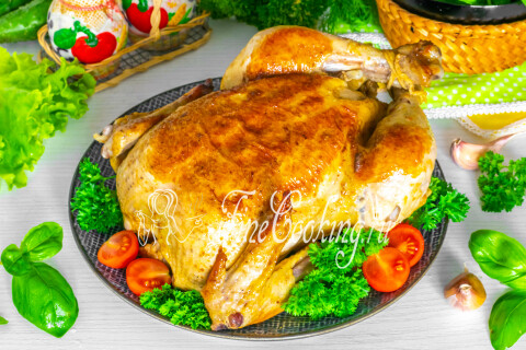 Румяная запечённая курица целиком на блюде с гарниром и зеленью.