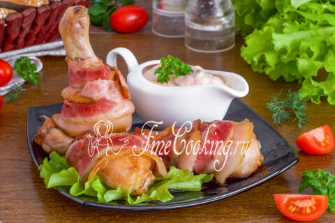 Куриные ножки, запечённые в беконе, поданные на тарелке с соусом.