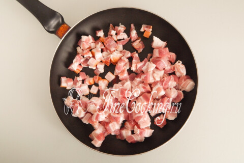 Кусочки грудинки в широкой сковороде под крышкой на плите.