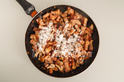 Пшеничная мука, насыпанная поверх мяса с грибами в сковороде.