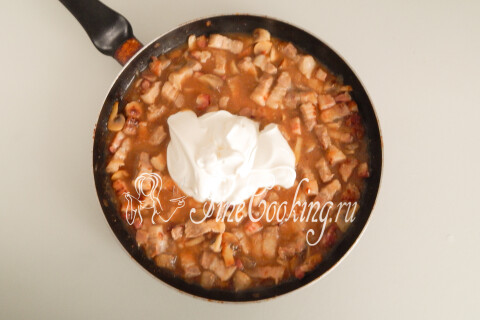 Сметана, вмешиваемая в мясной соус с грибами в сковороде.