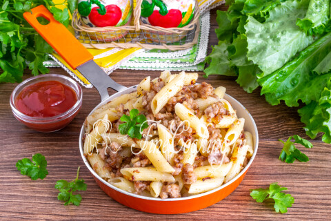 Макароны по-флотски с мясным фаршем на тарелке, посыпанные зеленью