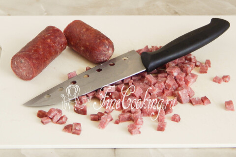 Колбаса копчёная, нарезанная мелким кубиком на доске.