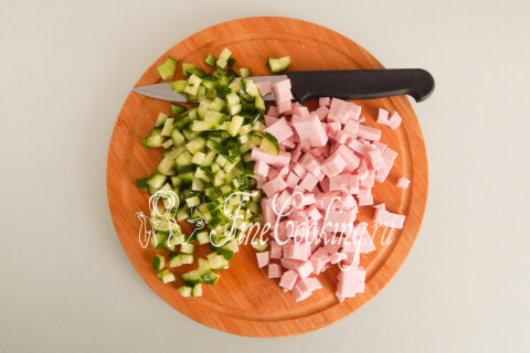 Варёная колбаса и огурцы, нарезанные мелким кубиком, на доске.