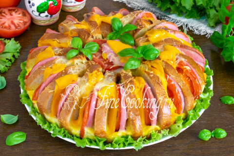 Пирог из батона с колбасой, сыром и помидорами на столе, готовый к подаче.
