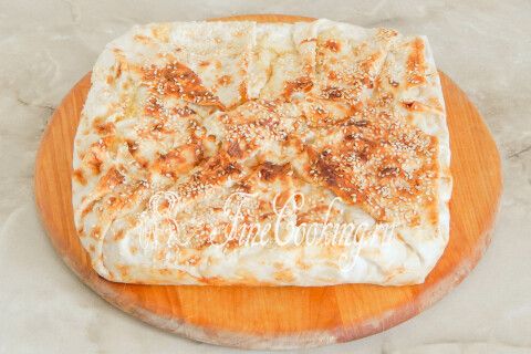 Испечённый лаваш с сыром нарезается порционными кусочками на разделочной доске