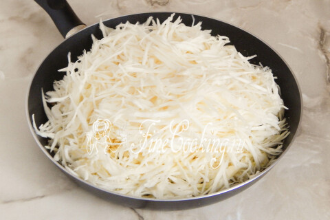 Нашинкованная капуста с луком, тушащаяся под крышкой в сковороде