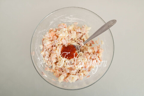 Салат с морепродуктами, перемешанный с ложкой красной икры в миске.