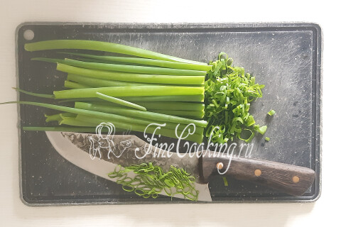 Зелёный лук, мелко нарезанный ножом, рядом варятся куриные яйца.