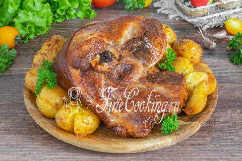 Румяная рулька с картошкой и зеленью на блюде.