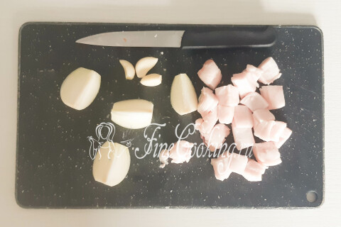 Свиное сало нарезано кусочками рядом с луком и зубчиками чеснока.