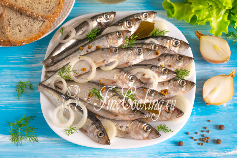 Готовая пряная салака на блюде рядом с чёрным хлебом и луком