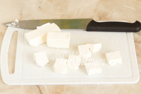 Брынза, нарезанная некрупными кусочками, на разделочной доске.