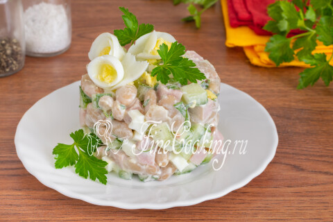 Готовый салат с фасолью, ветчиной, огурцами и яйцами в миске.