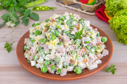Готовый салат с копчёной курицей, горошком и огурцом в тарелке.