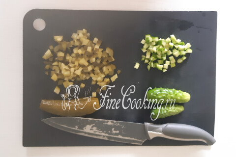 Маринованные и свежие огурцы, нарезанные мелким кубиком на доске.