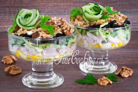 Слоёный салат с курицей и черносливом, украшенный розочками из огурца и петрушкой.