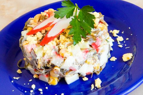 Салат с морской капустой и крабовыми палочками, поданный шайбочкой с желтком и зеленью