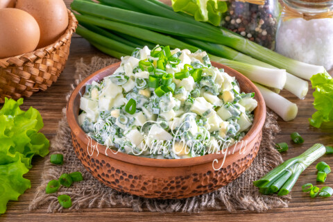 Салат с яйцом и зелёным луком, поданный в тарелке с обилием свежей зелени.
