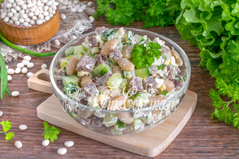 Готовый салат с языком, фасолью и огурцом в тарелке на столе.