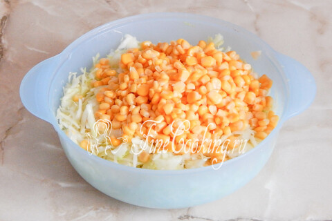 Капуста разминается руками с солью рядом с консервированной кукурузой