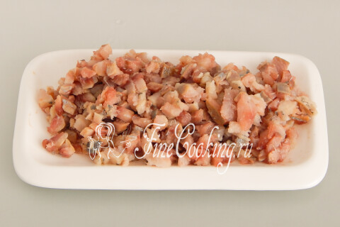 Сельдь, нарезанная мелким кубиком, на разделочной доске