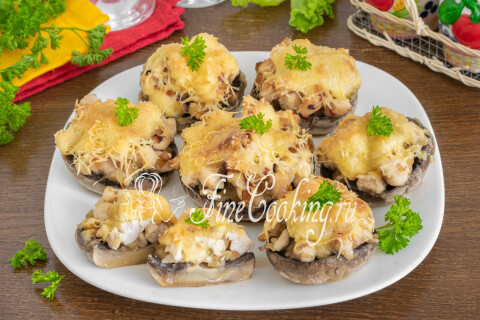 Готовые шампиньоны, фаршированные курицей и сыром, поданы горячими на тарелке