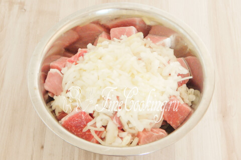 Мятый лук с соком, перекладываемый к кускам свинины в миске.