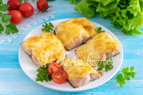 Запечённая горбуша под сырной корочкой на тарелке с овощами и зеленью.