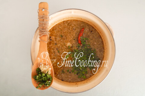 Кастрюля супа, накрытая крышкой, с зеленью и чесноком