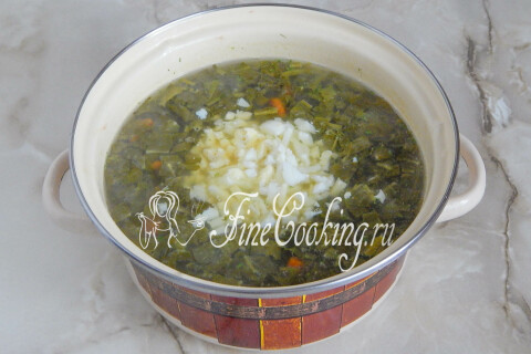 Кастрюля с супом, рубленым яйцом и щавелем на плите