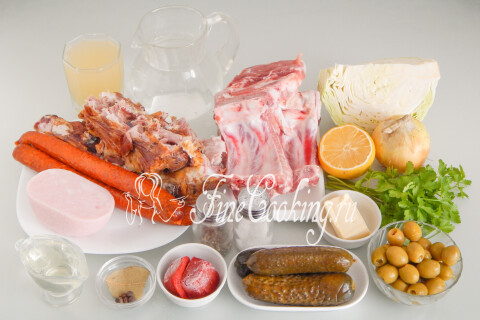 Продукты для мясной солянки: свинина, копчёные рёбра, ветчина, колбаски, капуста, солёные огурцы, лук, томатный соус и лимон.