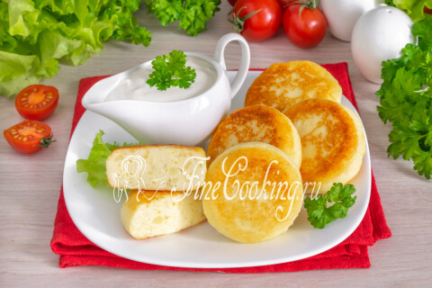 Румяные картофельные сырники на тарелке со сметаной.