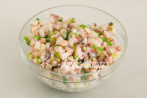 Сельдь, перемешанная с зелёным луком, в миске под пищевой плёнкой.