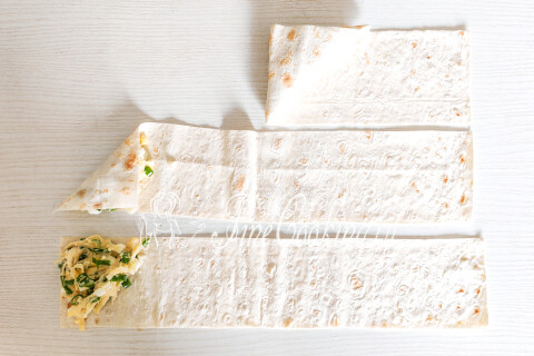 Полоска лаваша с начинкой на краю, сложенная в форму треугольника.