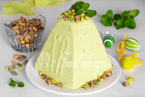 Творожная пасха фисташковая на тарелке с кусочками орехов внутри.