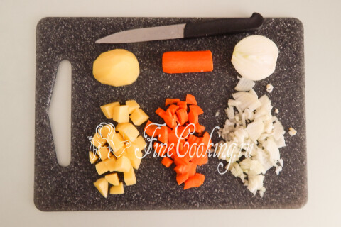 Картофель, морковь и лук, нарезанные кубиками на разделочной доске