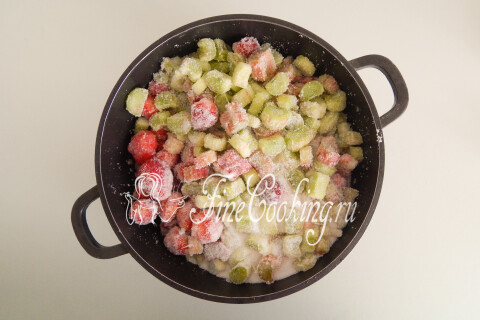 Кастрюля с клубникой, ревенем и сахаром, встряхиваемая на столе.