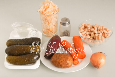 Свёкла, картофель, морковь, солёные огурцы, квашеная капуста, консервированная фасоль и репчатый лук на столе.