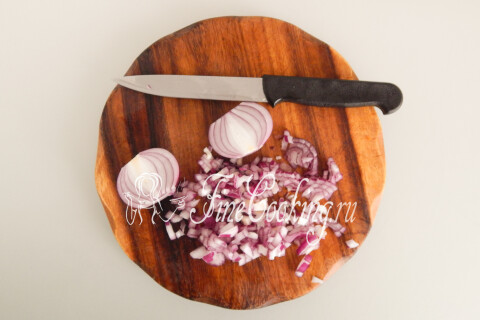 Репчатый лук, нарезанный мелким кубиком на разделочной доске.