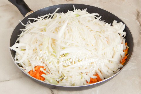 Капуста с луком и морковью в сковороде под крышкой, тушащаяся до мягкости.