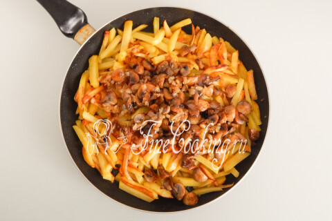 Обжаренные шампиньоны с луком, добавленные к картофелю в сковороде.